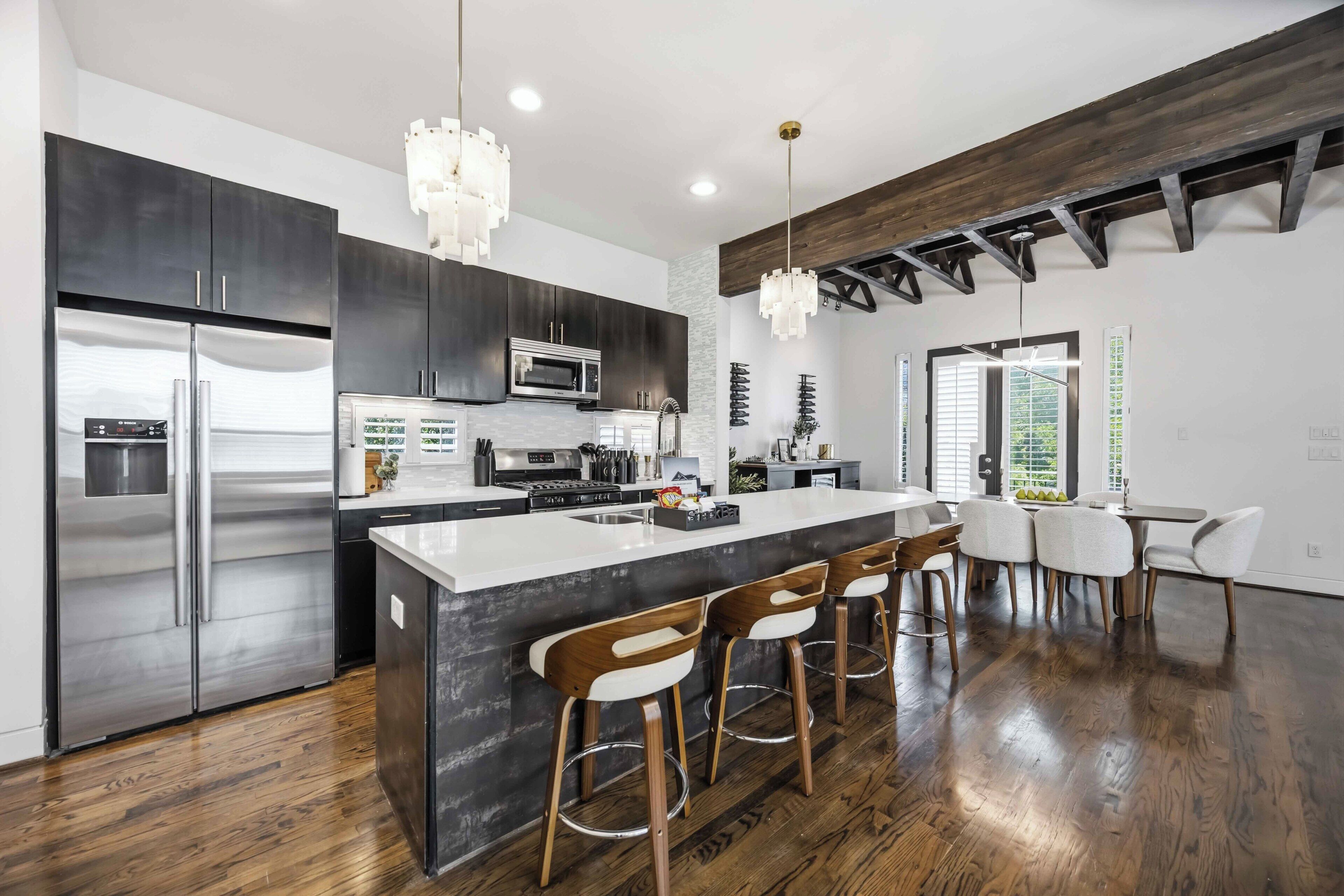 A modern kitchen with stainless steel appliances, a marble island, and bar stools.