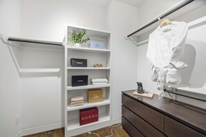 A walk-in closet with shelves containing luxury brand boxes, a wooden dresser, and a hanging robe. - The Crawford HTX: Houston luxury with style, rooftop views, & local flair. (Houston)