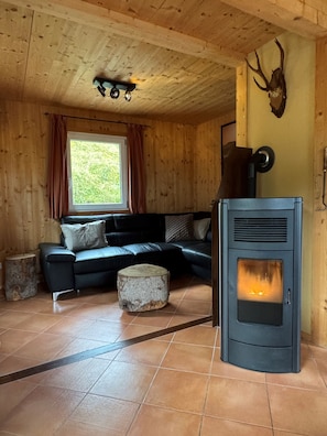 A cozy room with a black sofa, a stone ottoman, and a wood-burning stove. - Chalet # 49 with 3 BR for up to 8 people (Annaberg)