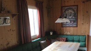 Puisella sisustuksella varustettu tila, jossa on vihreäverhoiltu penkki, puinen pöytä ja katosta roikkuva valaisin.