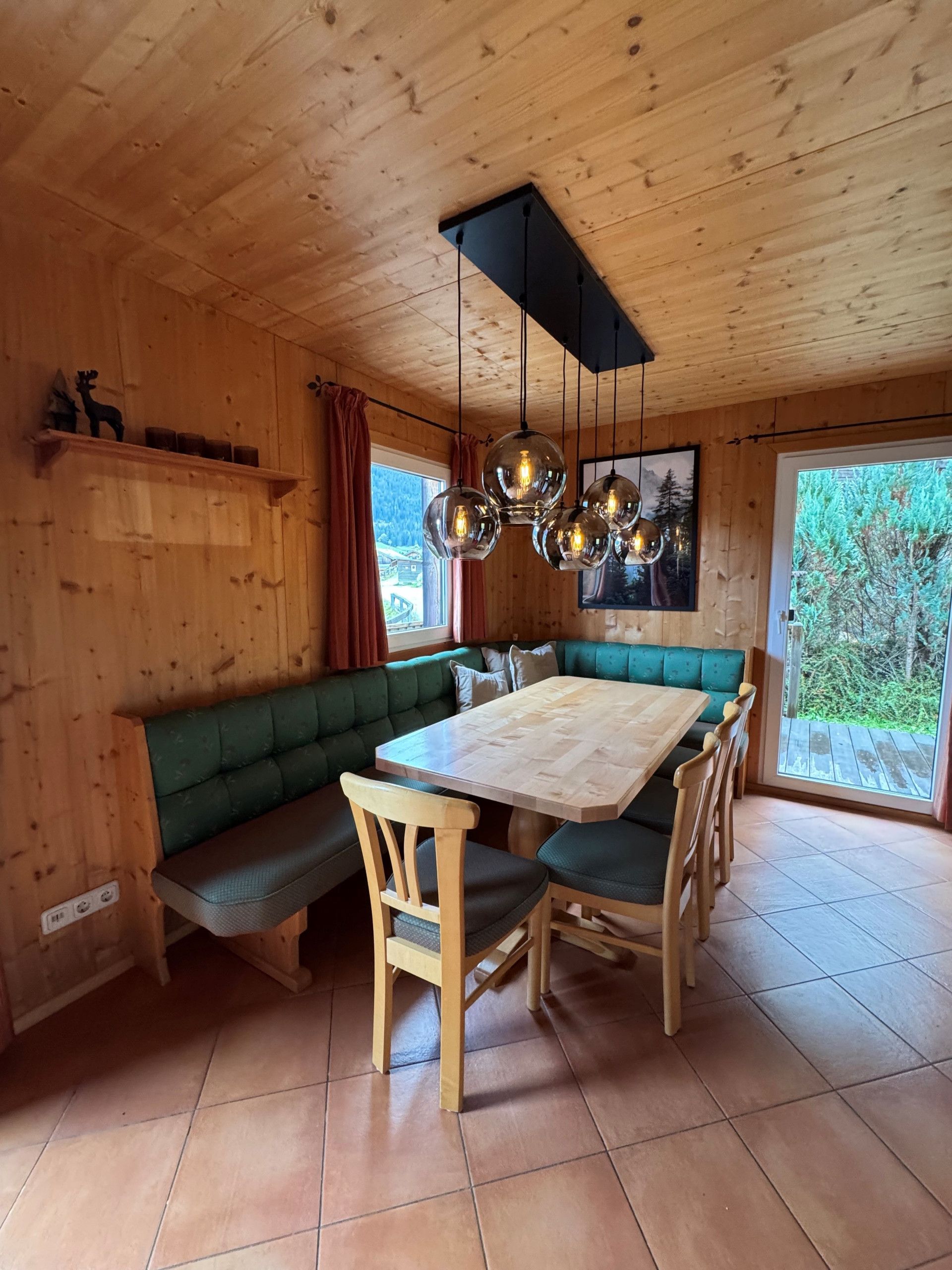 Een houten interieur met een groene, gestoffeerde bank, een houten eettafel en hangende, bolvormige lampen.