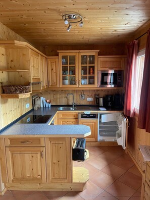 A kitchen with wooden cabinets, a built-in microwave, and a coffee maker. - Chalet # 49 with 3 BR for up to 8 people (Annaberg)