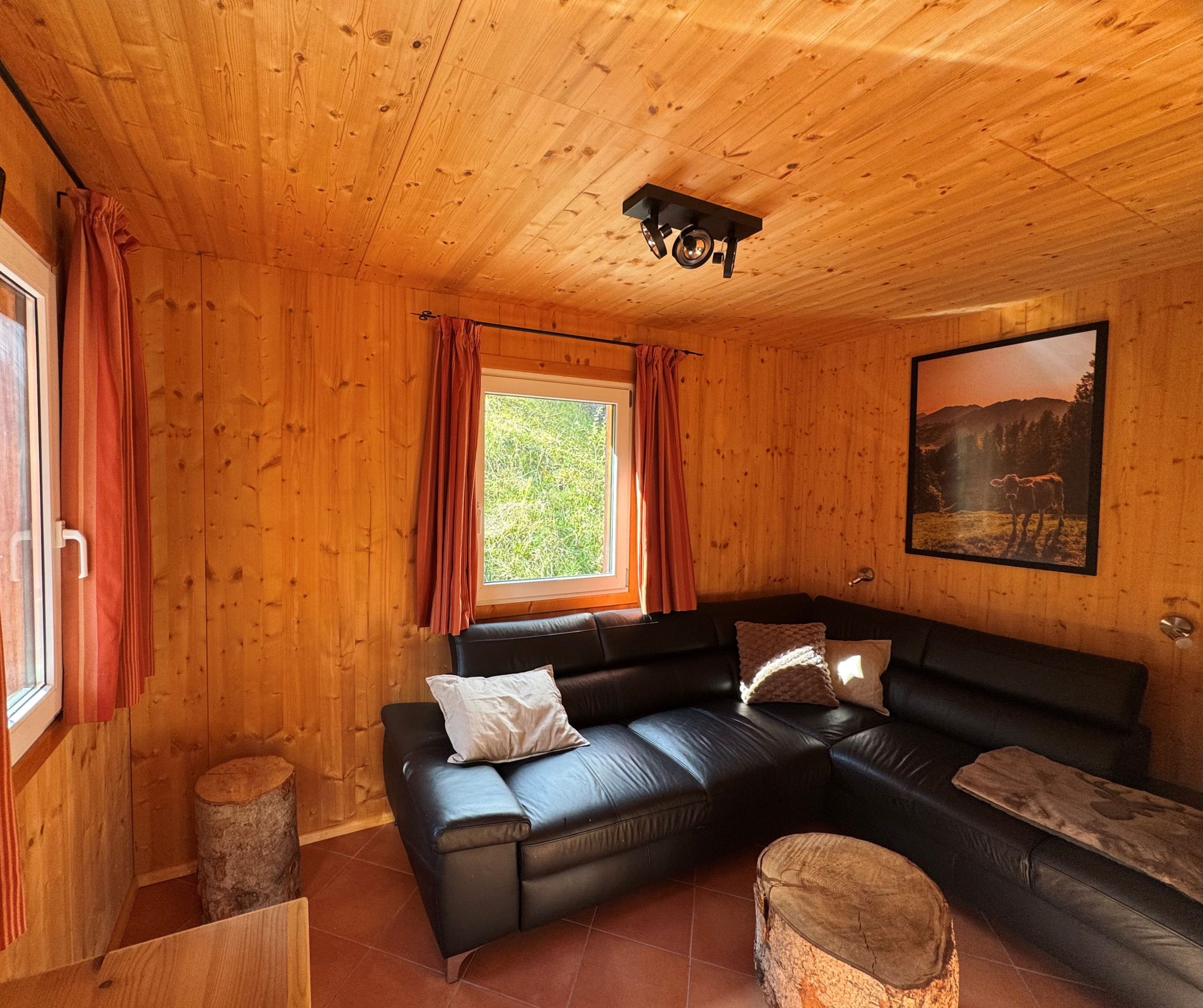 A wooden interior with a black leather sofa, a window with curtains, and a framed picture on the wall.