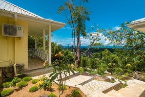 A covered outdoor area with a view of a coastal landscape, featuring a paved patio and lush greenery.