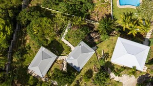 Vista aérea de um bairro residencial com três casas, piscina e vegetação densa.