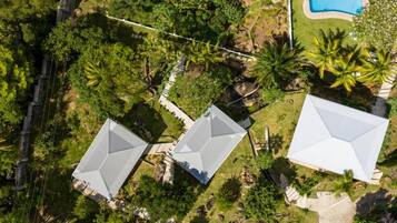 An aerial view of a residential area with three houses, a swimming pool, and dense greenery.