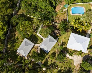 An aerial view of a residential area with three houses, a swimming pool, and dense greenery. - Naturalis Oceanview Residences (Victoria)