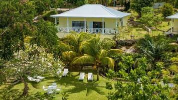 A pool surrounded by a lush garden, a white building with a balcony, and a view of a hillside with other buildings.