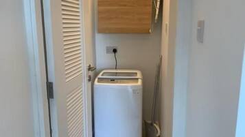 A narrow hallway with a washing machine, a wooden cabinet, and a broom leaning against the wall.