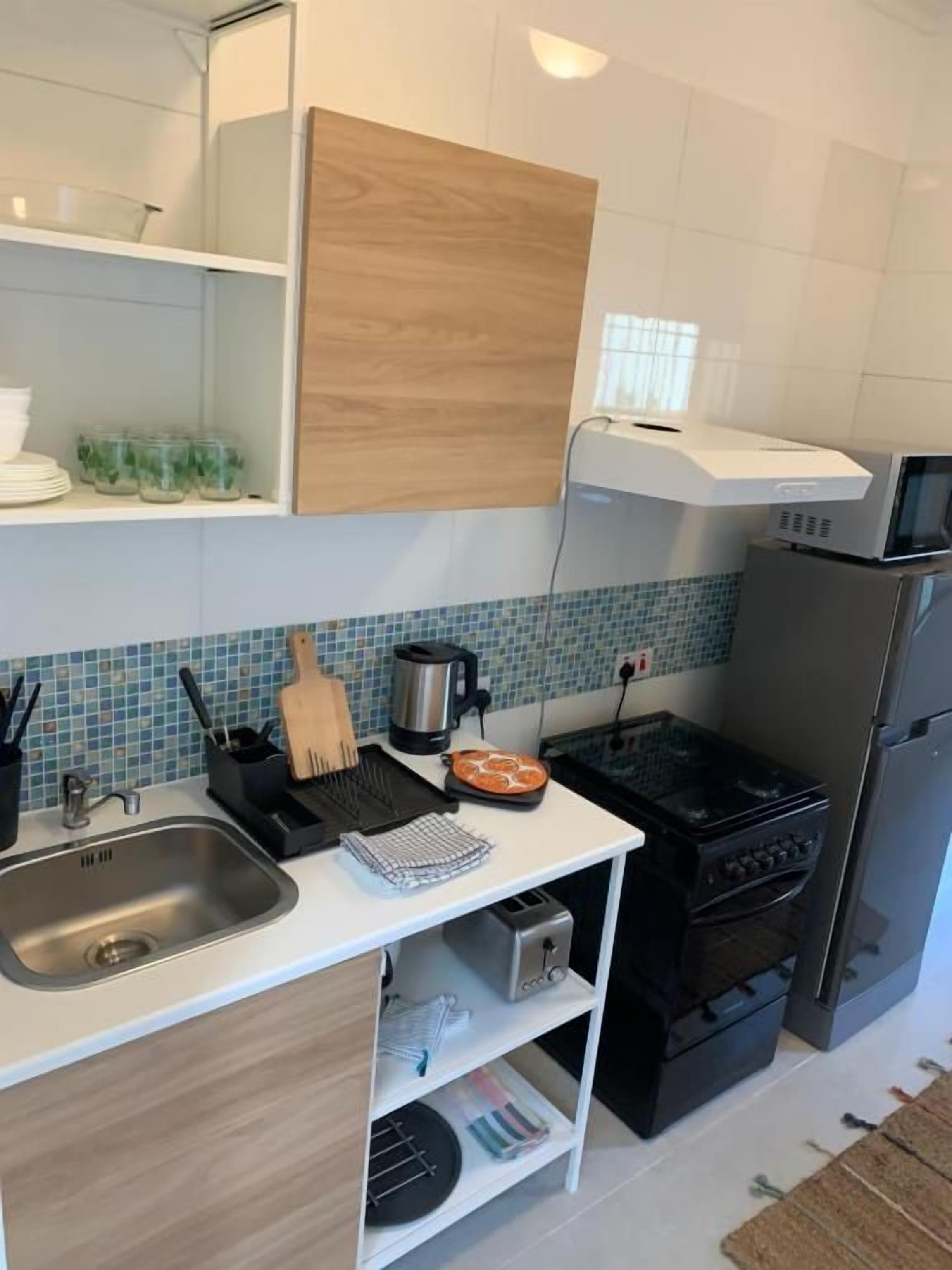 A compact kitchen with a microwave, toaster, and oven. There is a sink and a wooden cabinet above it.