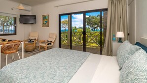 Quarto de hotel com cama, duas cadeiras, televisão, janela com vista e cortina.