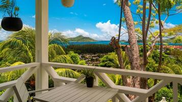 A white balcony with a view of a tropical landscape, including trees and a distant body of water.