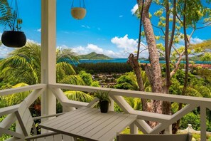 A white balcony with a view of a tropical landscape, including trees and a distant body of water. - Naturalis Oceanview Residences (Victoria)