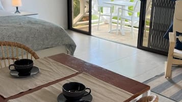 A room with a bed, a table with two cups, and a view of the outdoors through a glass door.