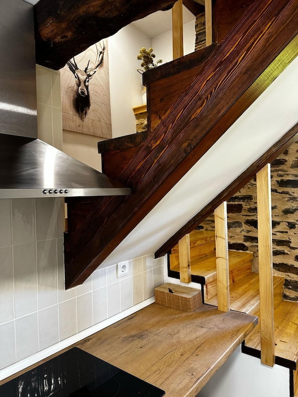 A kitchen with a wooden staircase, a stainless steel range hood, and a mounted deer head.