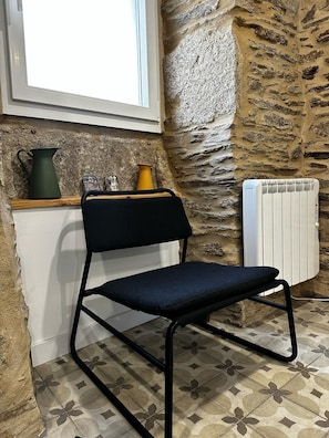 A chair with a black frame and seat, a radiator, a window, and a stone wall.