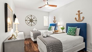 Un dormitorio con cama, mesitas de noche, ventilador de techo, televisor montado en la pared y decoración náutica.