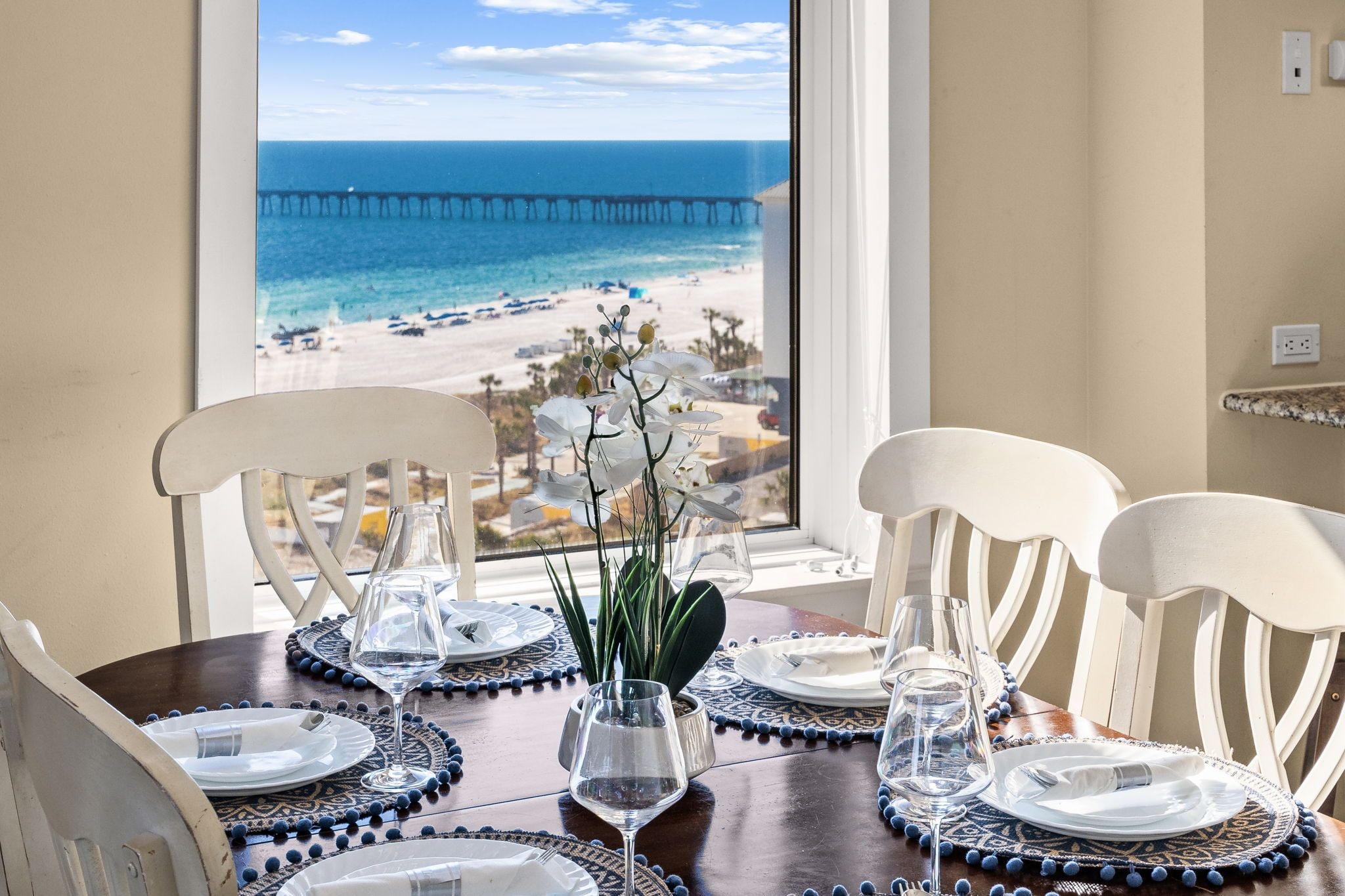A dining table set for four with a view of the beach and pier through a window.