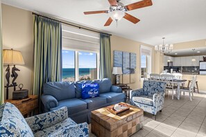 A spacious living room with a large window overlooking the ocean, a ceiling fan, and a dining area with a view. - Grand Escape! 3BR 3BA Sleeps 8 Gulf Views (Panama City Beach)