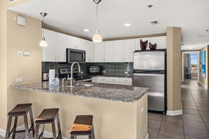 A modern kitchen with a granite countertop, stainless steel appliances, and a central island with bar stools. - Grand Escape! 3BR 3BA Sleeps 8 Gulf Views (Panama City Beach)