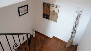 A staircase with a wooden handrail and a black metal railing, leading to a landing with a framed picture and a vase with branches.