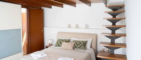 Un dormitorio con cama, una escalera de madera, una mesita de noche y una puerta.