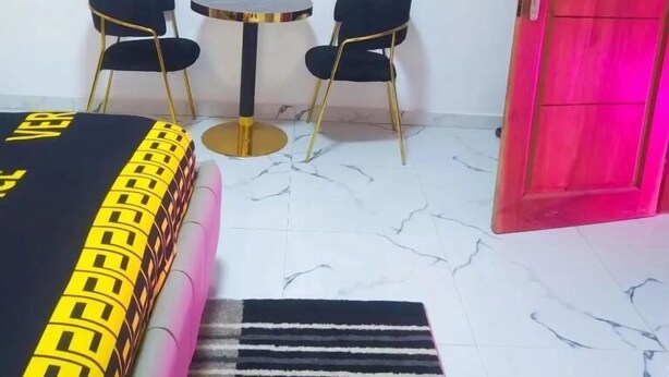 A hotel room with a bed, two chairs, a small table, a red door, and a marble floor. - Chambre SCAT urbam (Dakar)