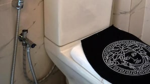 A toilet with a marble-patterned wall, a shower head, and a black mat with a circular design. - Chambre SCAT urbam (Dakar)
