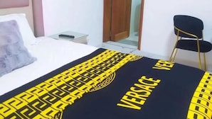 A hotel room with a bed, a chair, and a nightstand. - Chambre SCAT urbam (Dakar)