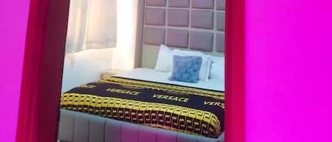 A room with a bed, a window with curtains, and a headboard with a patterned design.