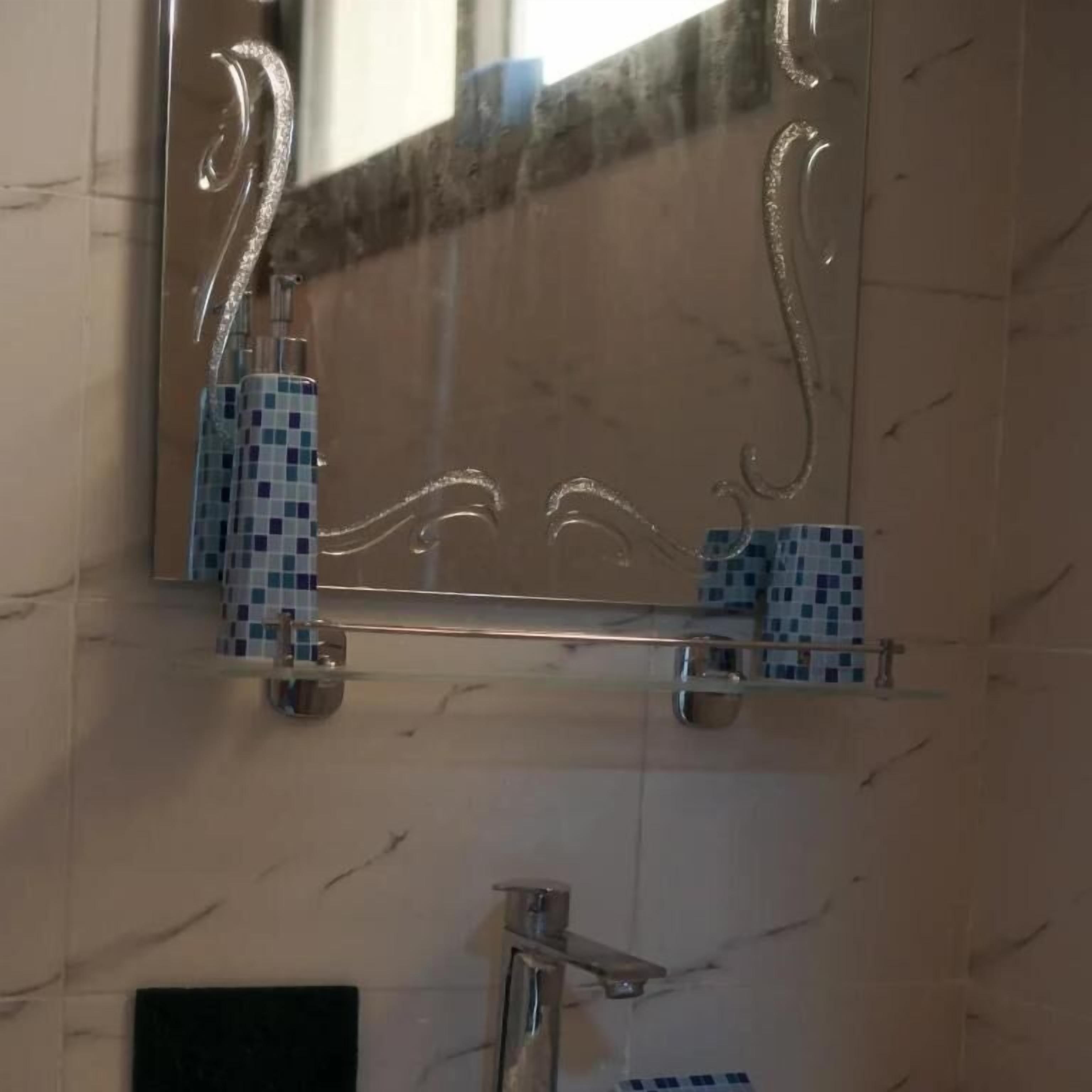 A bathroom with a marble wall, a mirror, and a shelf with a blue mosaic tile.