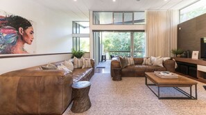 A modern living room with leather sofas, a coffee table, and a large window overlooking greenery. - Little Cove Luxury Escape (Noosa Heads)