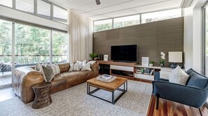 A modern living room with a leather sofa, a coffee table, and a TV. - Little Cove Luxury Escape (Noosa Heads)