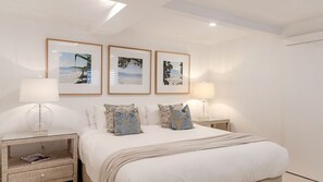 A bedroom with a bed, two bedside tables, and three framed pictures on the wall. - Little Cove Luxury Escape (Noosa Heads)