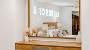 A hotel room with a large mirror, a bed with pillows, a bedside table with a lamp, and a vase with dried flowers. - Little Cove Luxury Escape (Noosa Heads)
