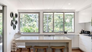 Una cucina moderna con isola centrale, due sgabelli e ampie finestre vista su un'area verde.