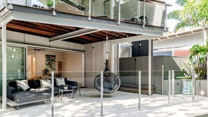 A modern outdoor living space with a glass enclosure, a hanging decorative piece, and a seating area with cushions. - Little Cove Luxury Escape (Noosa Heads)