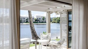 A balcony with a view of a body of water, a palm tree, and a building in the background. - Bella Vista Waterfront Luxury (Noosaville)