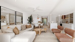 Ein modernes Wohnzimmer mit Sofa, Couchtisch und Sesseln, ein Essbereich mit Tisch und Stühlen sowie eine Küchenzeile mit Schränken und Arbeitsplatte.