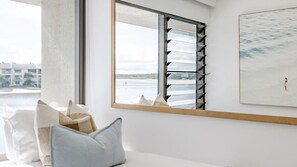 Ein Zimmer mit einem großen Fenster, Blick auf ein Gewässer und einem Bild an der Wand.