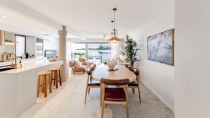 Eine moderne Küche mit Kochinsel, Essbereich mit rundem Tisch und Stühlen sowie ein großes Fenster mit Blick ins Freie.