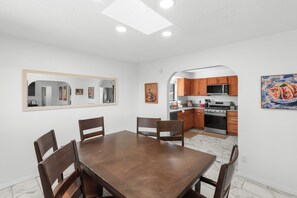 Un comedor con mesa y sillas de madera, una cocina con muebles de madera y electrodomésticos modernos, y un espejo grande en la pared.