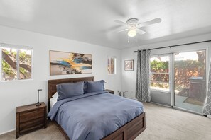 A bedroom with a bed, a nightstand, a ceiling fan, a window, and a door leading to a patio.
