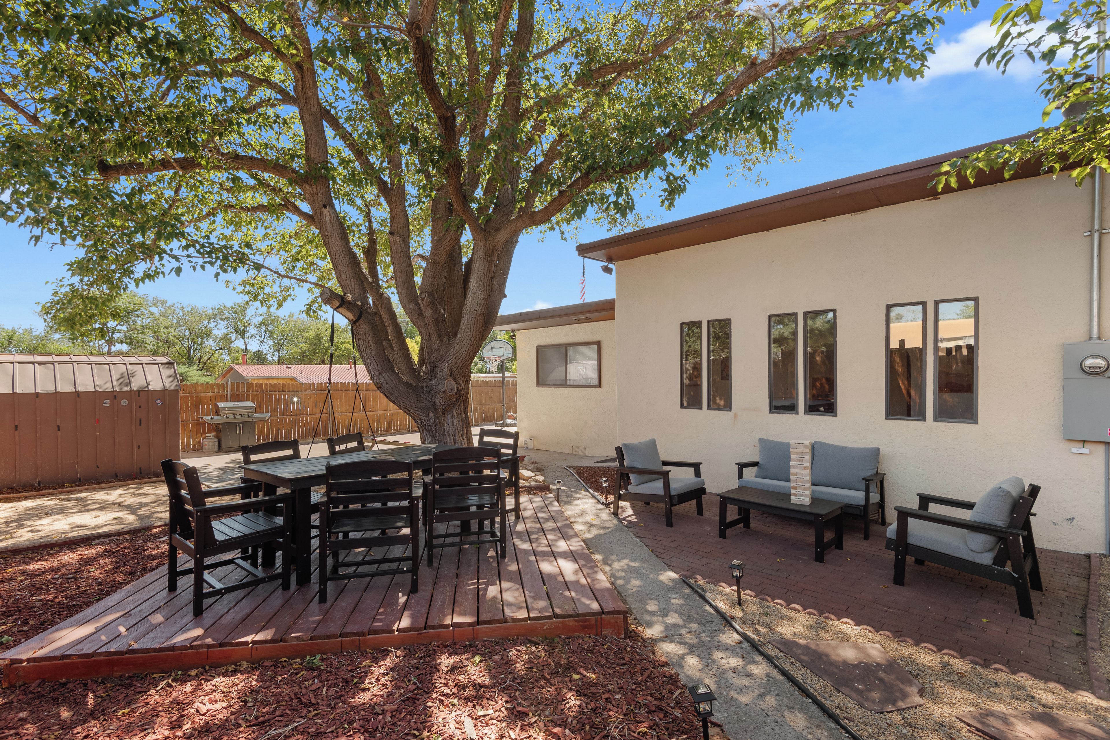 Un patio exterior con una mesa y sillas de madera, una hamaca y un aro de baloncesto.