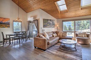 A spacious living room with a wooden ceiling, a large sofa, a dining table with chairs, and a view of a mountainous landscape through the windows. - Updated Animas Valley Condo with Awesome Views - 2 Decks (Durango)