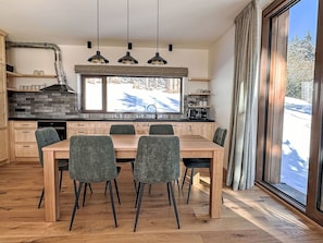 Eine moderne Küche mit großem Esstisch, Holzschränken und Blick auf eine verschneite Landschaft.