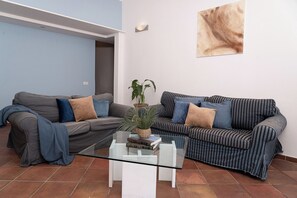 Uma sala de estar com dois sofás, uma mesa de centro de vidro e uma planta em vaso.