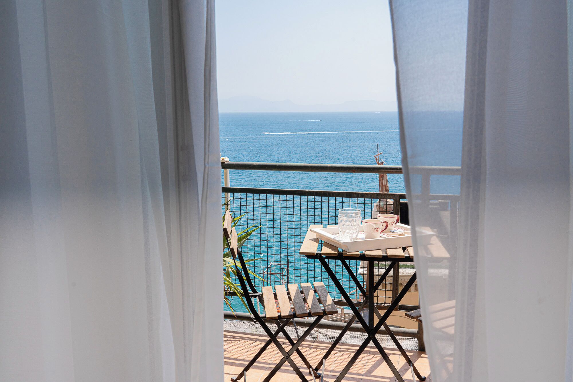 Un balcon avec vue sur la mer, une table avec un plateau et une chaise.