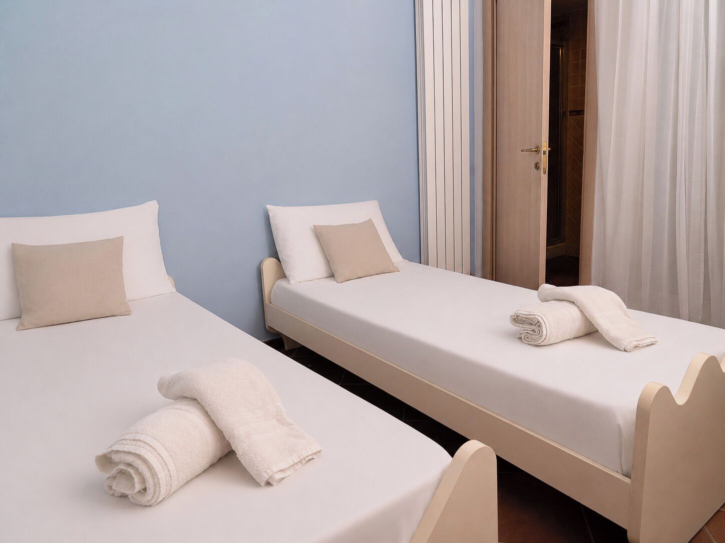 Two single beds with white linens and beige pillows in a room with light blue walls.