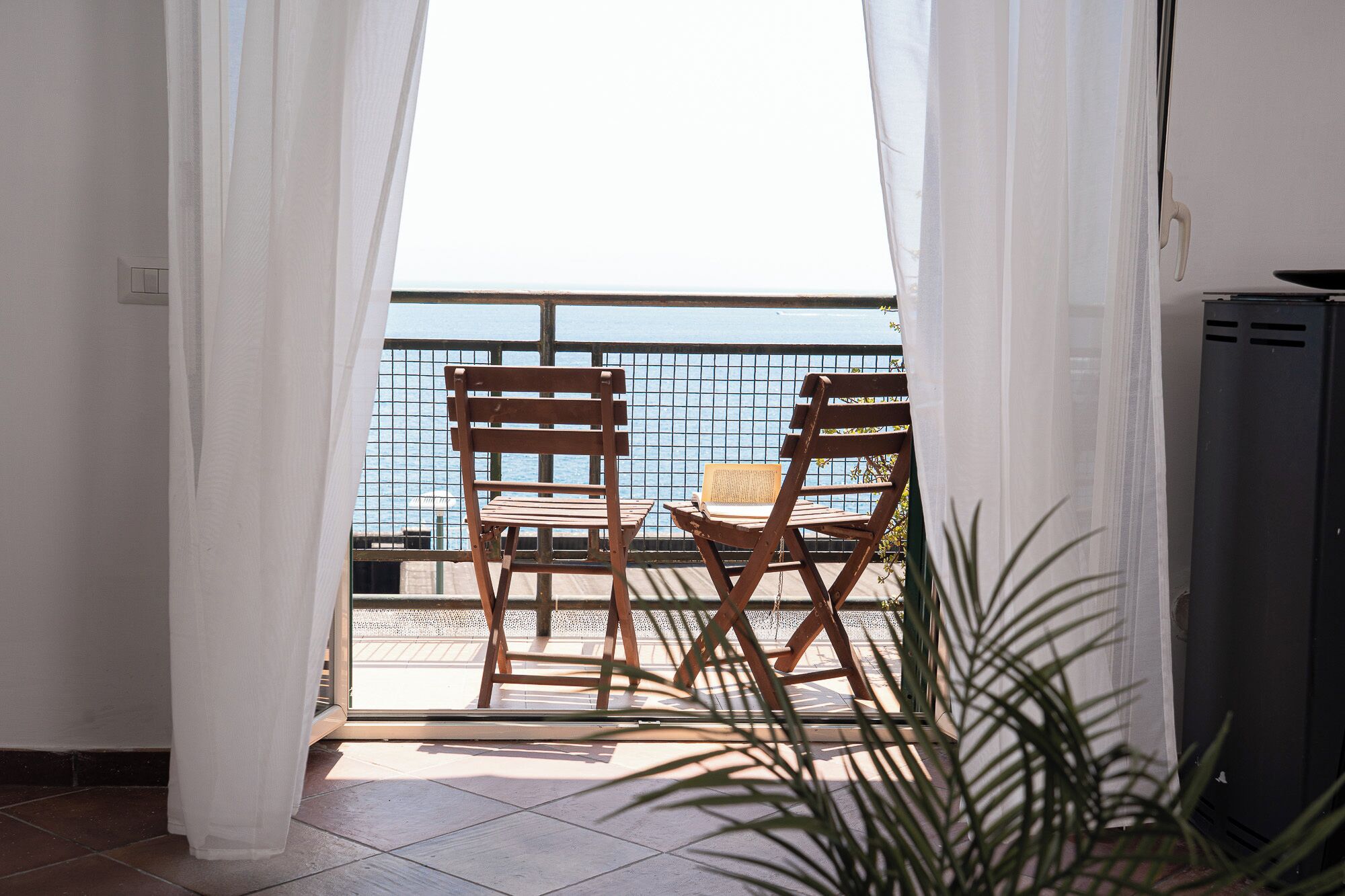 Un balcon avec deux chaises en bois et une table, une rambarde en métal et un pot de fleurs.